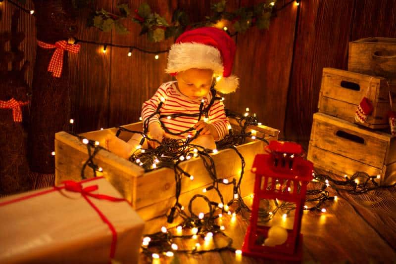 Cute child in Santa Hat sitting in box and playing with Christmas lights