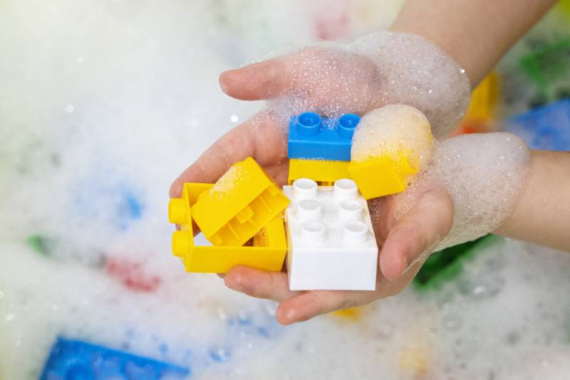 Child hands with colorful bright construction blocks in soap foam water
