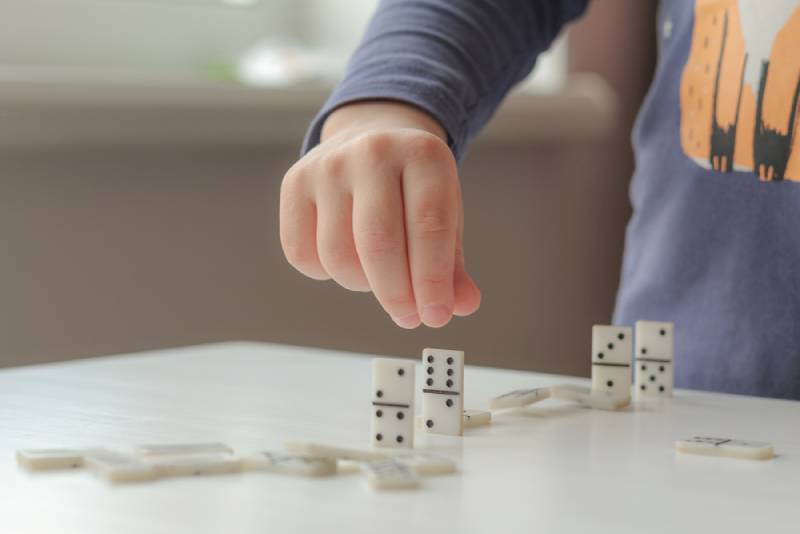 Kid playing with dominoes on white table