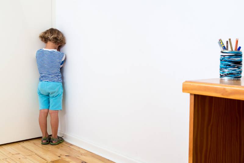 Kid in blue shirt and shorts standing in the corner