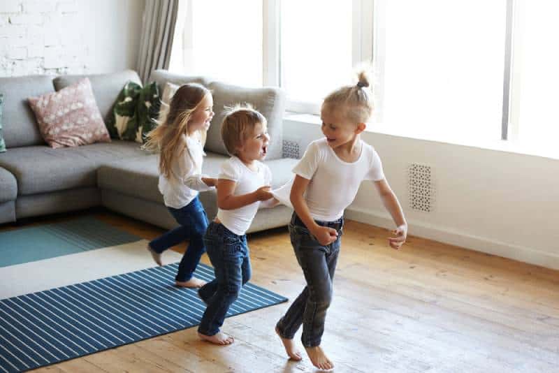 three happy joyful children one girl and two boys pullin each other by clothes while dancing at home