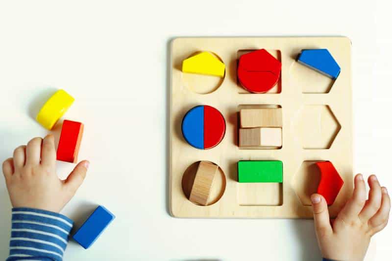 little Montessori kid learning about color, shape, sorting, arranging by engaged colorful wooden sensorial blocks