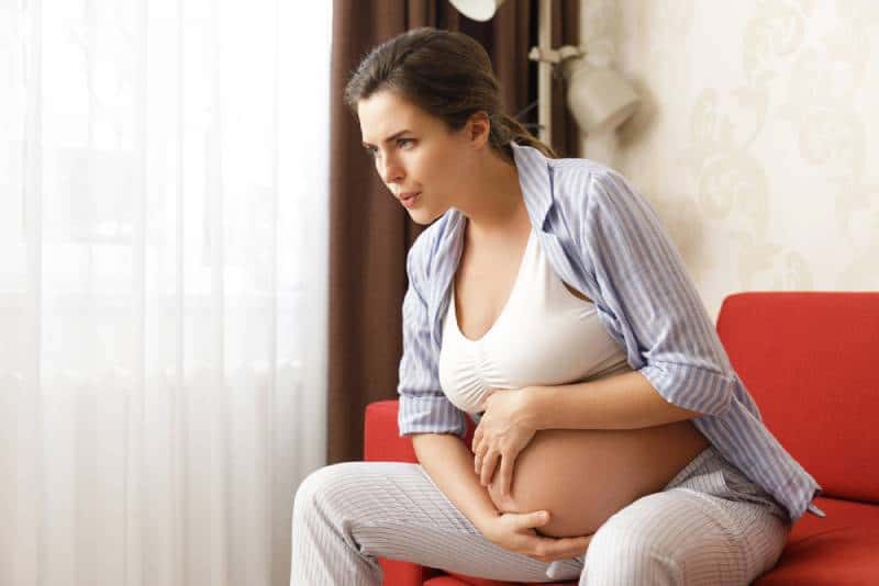 Pregnant woman at home feels sick while holding her belly