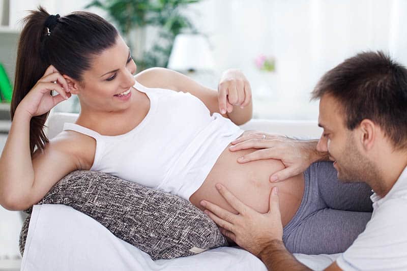 pregnant woman lying and man feeling baby moving in belly