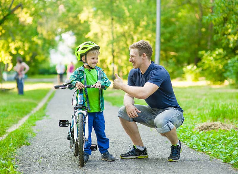 father and son enjoying a nice day outside in the park kid learning how to ride a bike