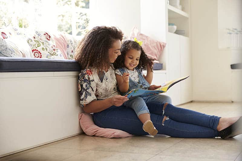 mother and daughter sitting on floor reading a book rie parenting method