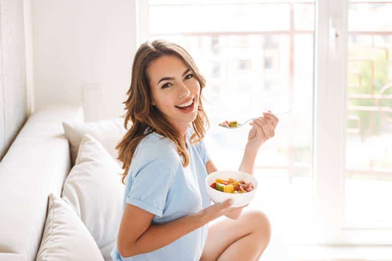 woman eating healthy breakfast while sitting on a couch at home