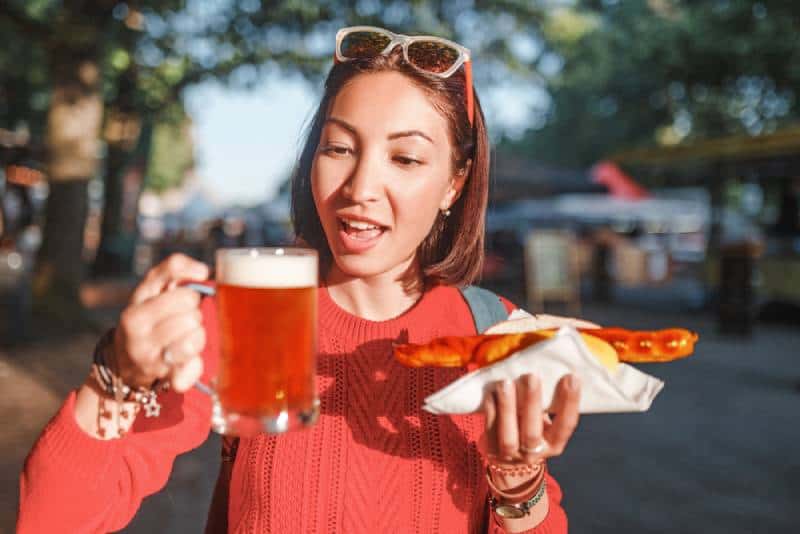 girl enjoys snacking on junk food - hot dog with fried sausage and beer