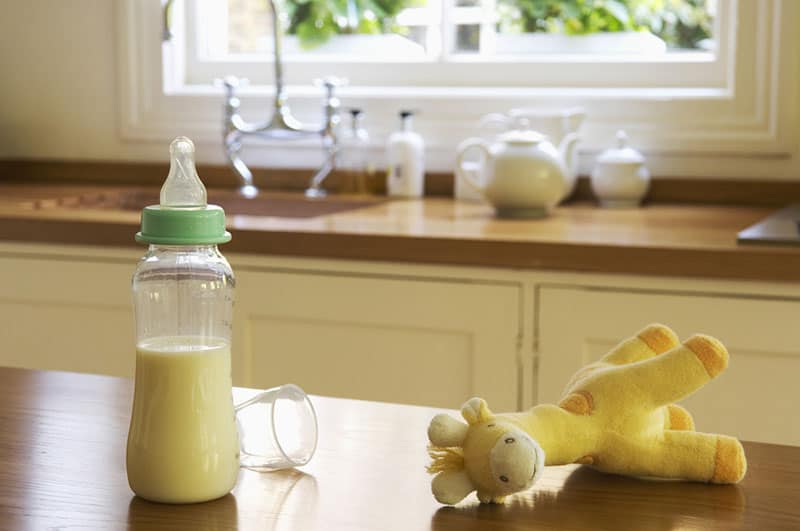 baby bottle with milk and a toy on the table in the kitchen