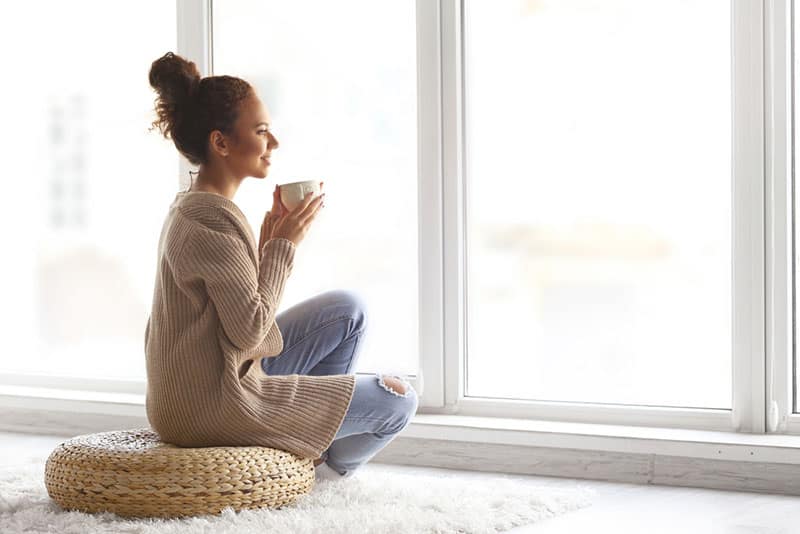 beautiful young woman drinking coffee and looking through window