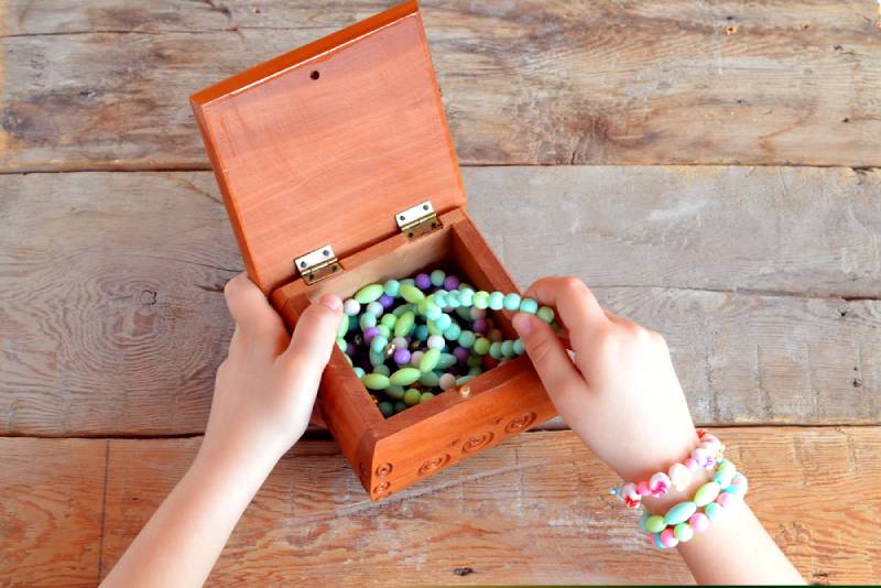 Little girl opens a box of bracelets on wooden background