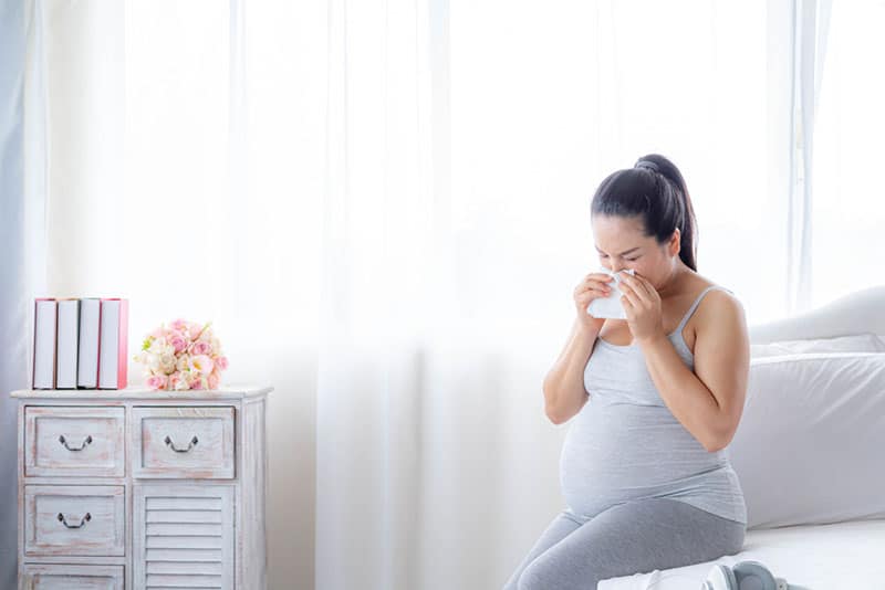 pregnant woman blowing running nose in bedroom