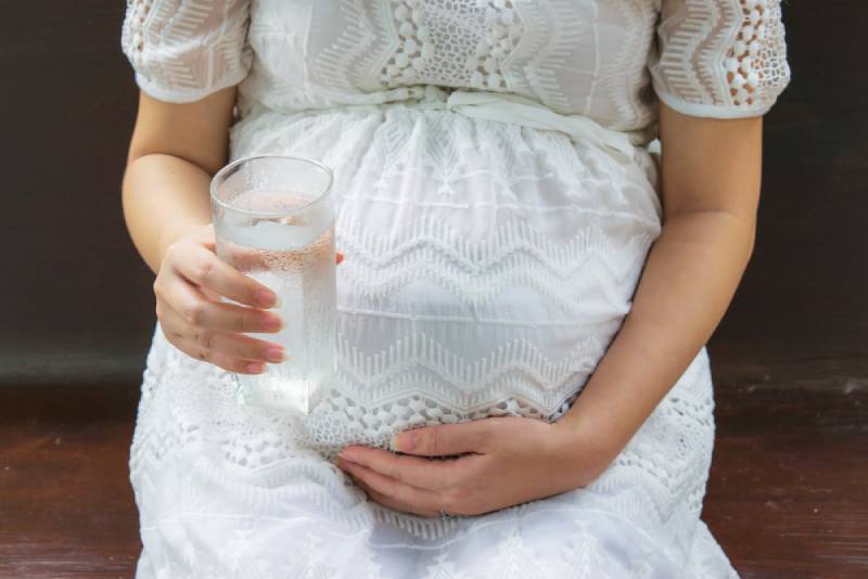 Pregnant woman holding her belly and with a glass of water
