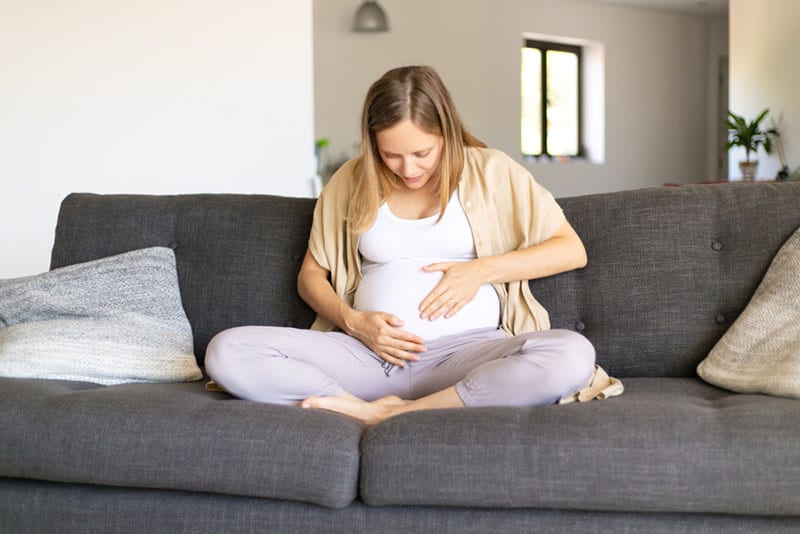 pregnant woman touching her belly while sitting on the couch