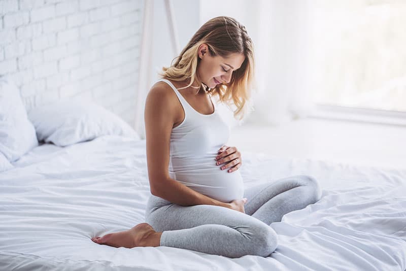 pretty pregnant woman sitting on the bed and feels the baby moving inside