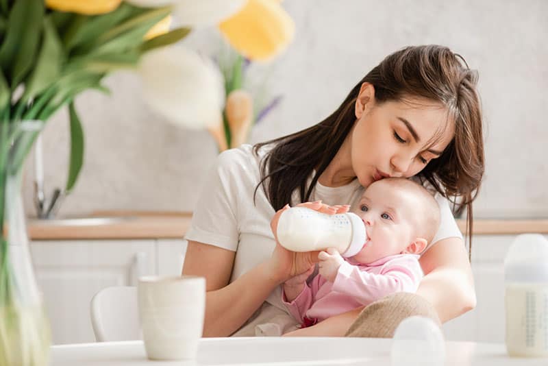 pretty woman kissing her baby in head and feeding with bottle of milk