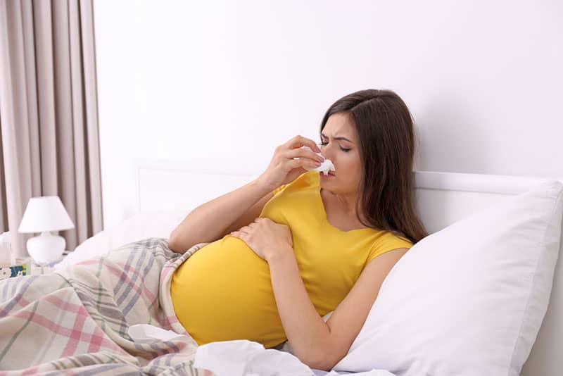sick pregnant woman lying in bed at home