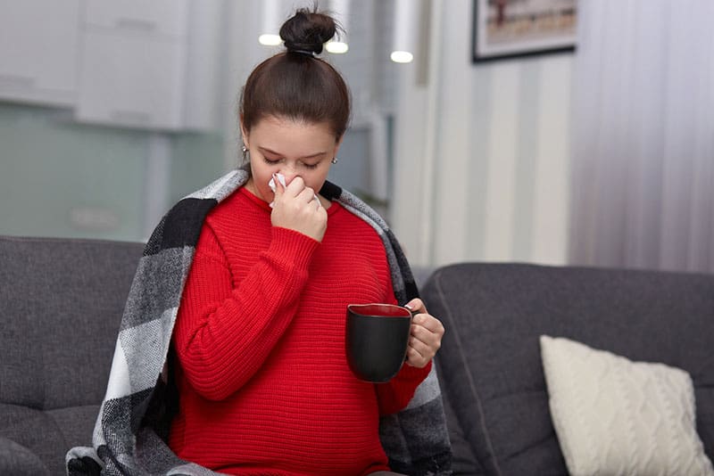 sick pregnant woman with stuffy nose holding cup of tea