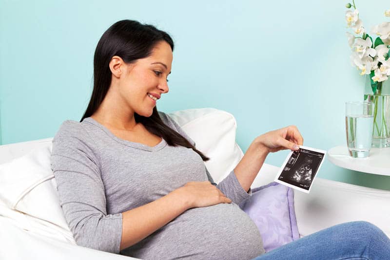 beautiful pregnant woman looking at ultrasound picture of her baby