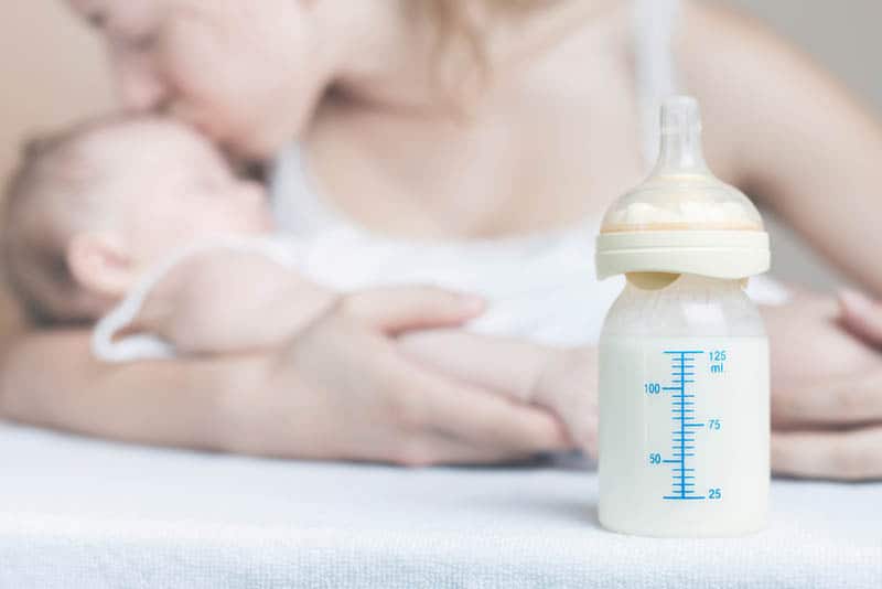 bottle of breast milk and mother kissing a baby in backgroung