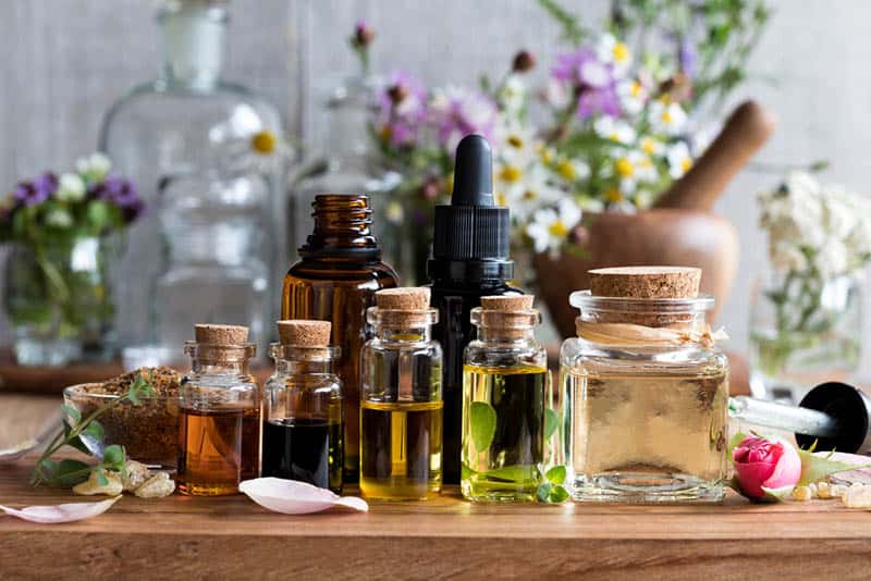 bottles of essential oils on the table with herb and flowers in background