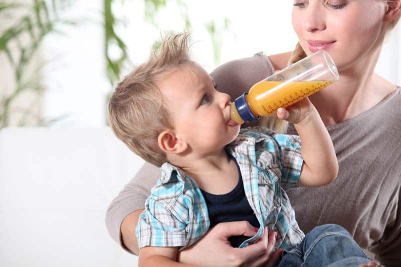 cute boy drinking juice from bottle and sitting on mother