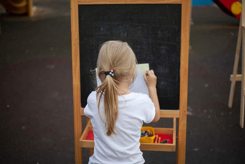 little girl sitting and trying to paint on the easel