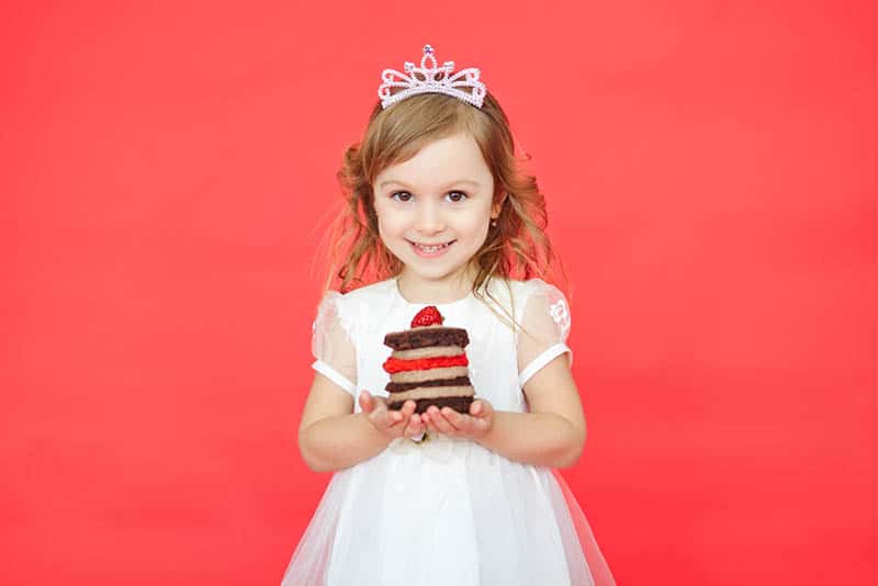 little girl with crown on the head holding a piece of cake