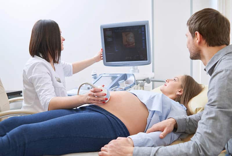 loving couple with doctor looking at ultrasound monitor
