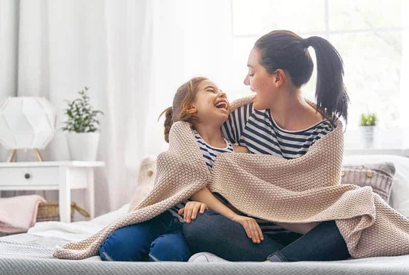 mother and daughter laughing covered with blanket