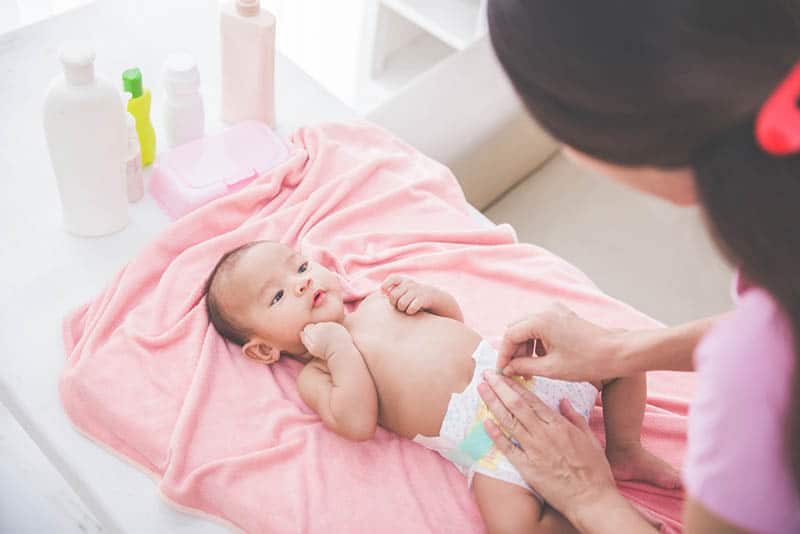 mother changing diaper to cute baby girl