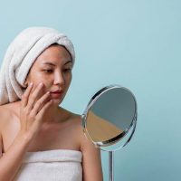 Woman in a towel touching her face in front of the mirror