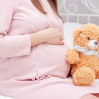 pregnant woman with teddy bear sitting on bed