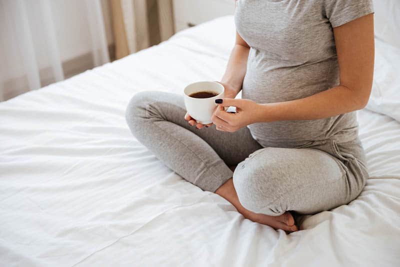 pregnant woman drinking coffee on the bed