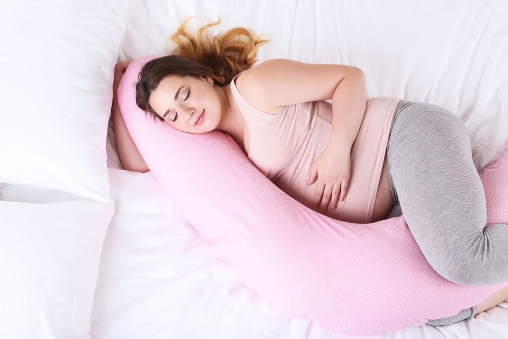 pregnant woman lying with pregnancy pillow on the bed