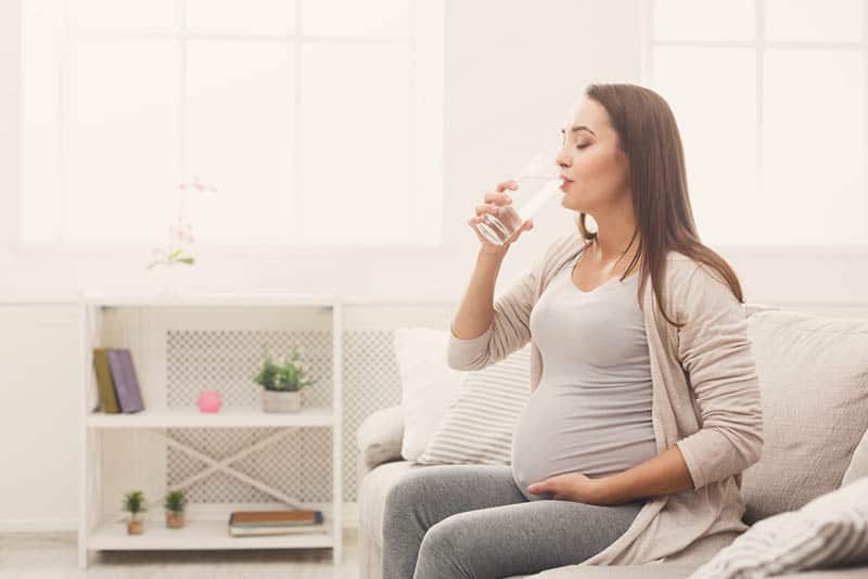 pregnant woman sitting on the bed and drinking water