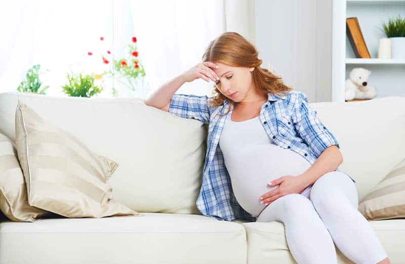 worried pregnant woman sitting on the couch