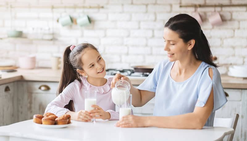 oung mother talking to a girl and putting milk in a glass