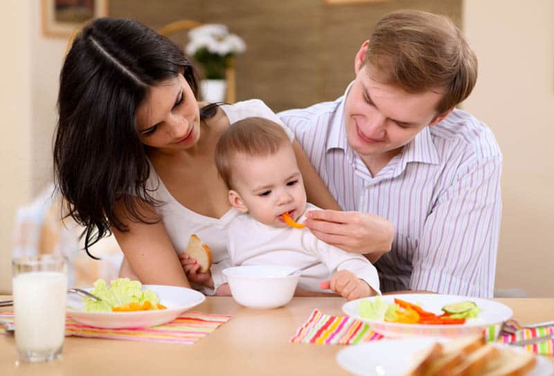 young parents feeding their child with vegetables