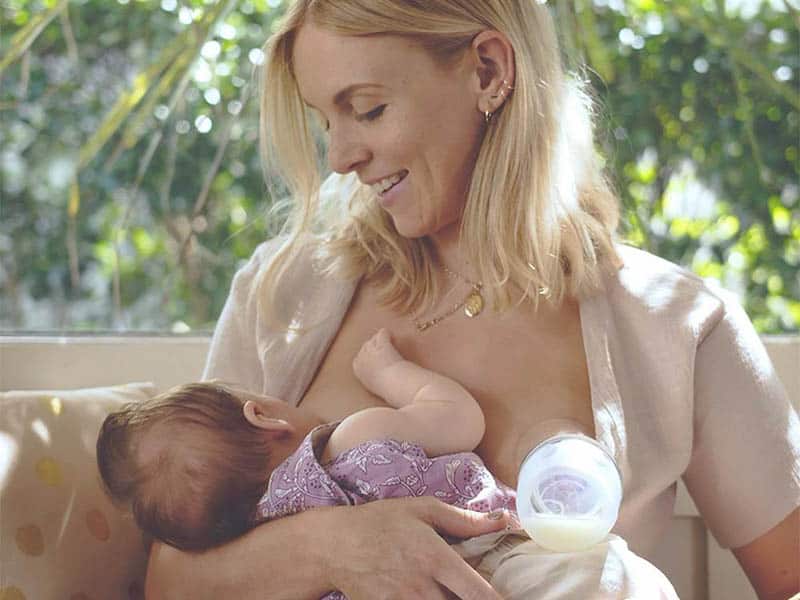 young woman breastfeeding baby and using haakaa breast pump