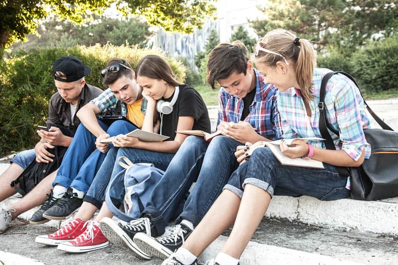 a group of teenagers sitting outdoor and holding phones