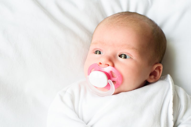 adorable baby lying on white sheets and sucking pacifier