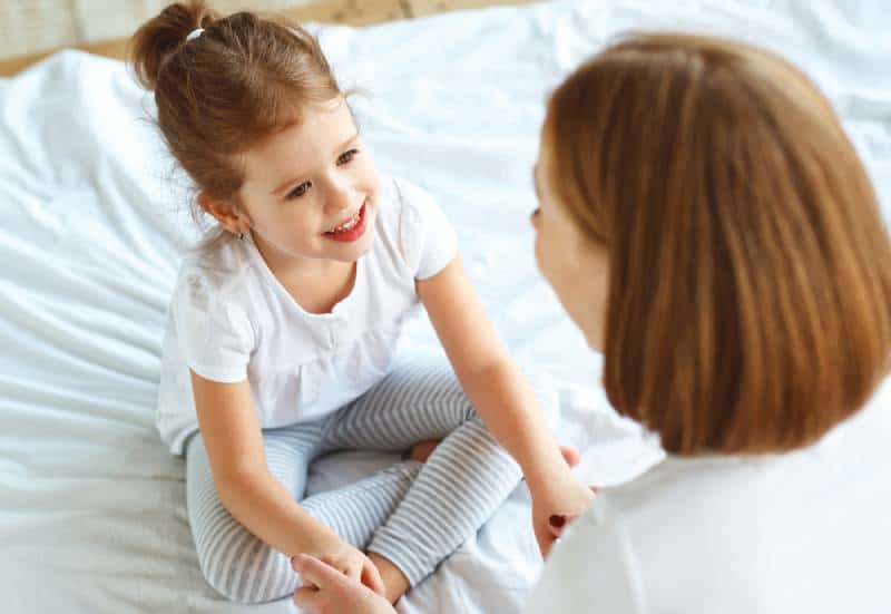 adorable little girl talking with mother on the bed