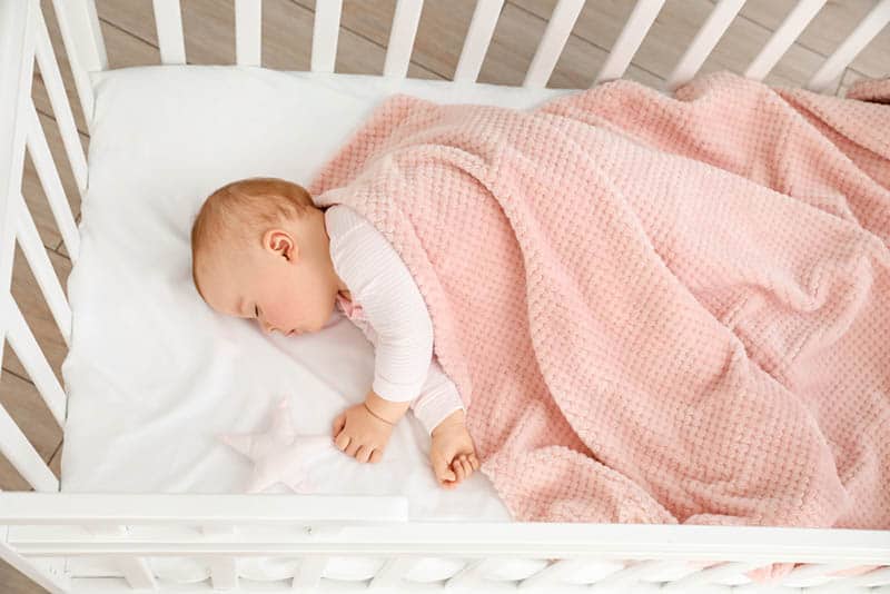 baby sleeping in crib covered with pink blanket