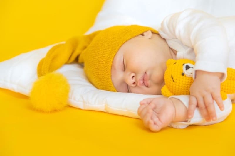 baby sleeping with a yellow hat and teddy bear