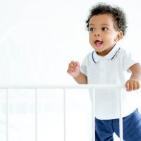 toddler boy standing in bed holding a bed rail