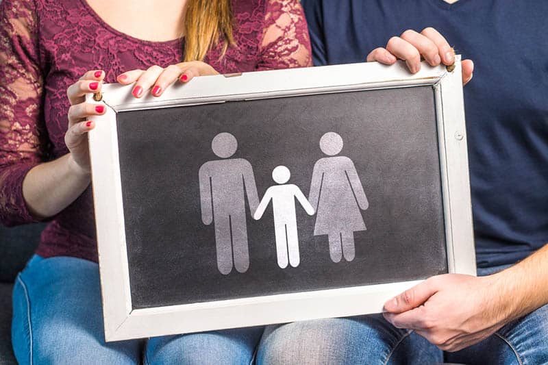 couple holding blackboard with drawing of family on it