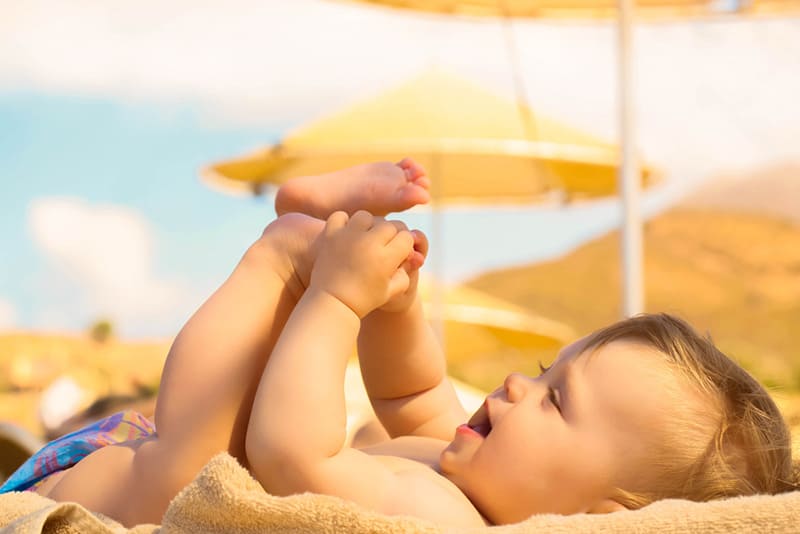 cute baby lying in sand on the beach and playing with feet 