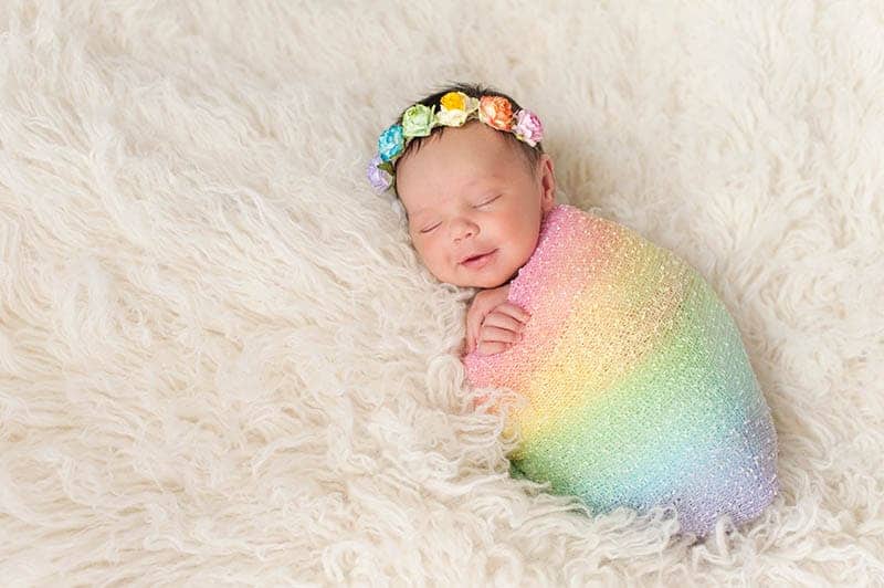 cute newborn baby wrapped into colorful blanket with flower crown on the head