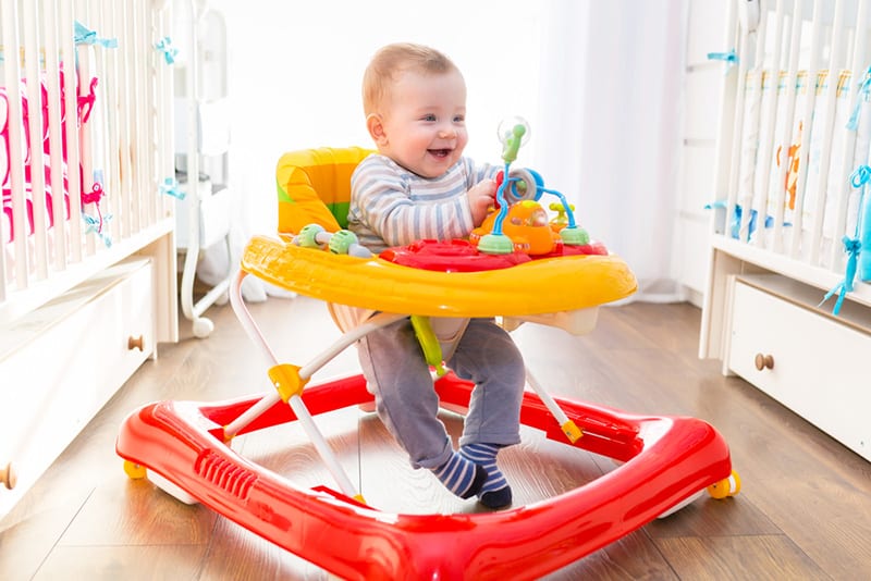 cute smiling baby sitting in colorful walker in the room